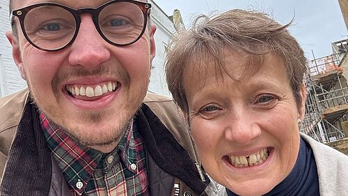 Adam Dance MP smiles for a selfie with Police and Crime Commissioner Clare Moody outdoors on a cloudy day, with buildings and scaffolding in the background