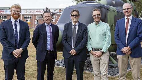 Adam Dance MP stands with four people in front of a military helicopter at Leonardo's Yeovil site