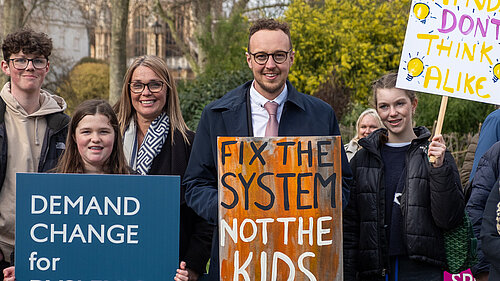 Adam Dance MP stands outside Parliament with campaigners holding signs calling for better support for dyslexic children. One sign reads “Fix the system, not the kids”.