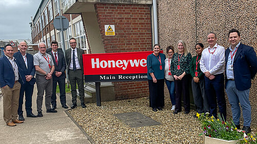 A group of employees and visitors stand outside the Honeywell main reception building beside a large company sign