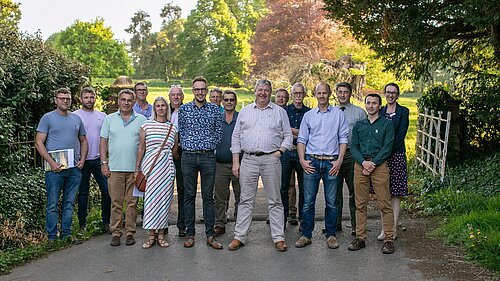 A group of around 16 people, including Adam Dance MP and Alistair Carmichael MP, standing outdoors on a tree-lined path during a sunny afternoon, gathered for a rural issues forum in Somerset.